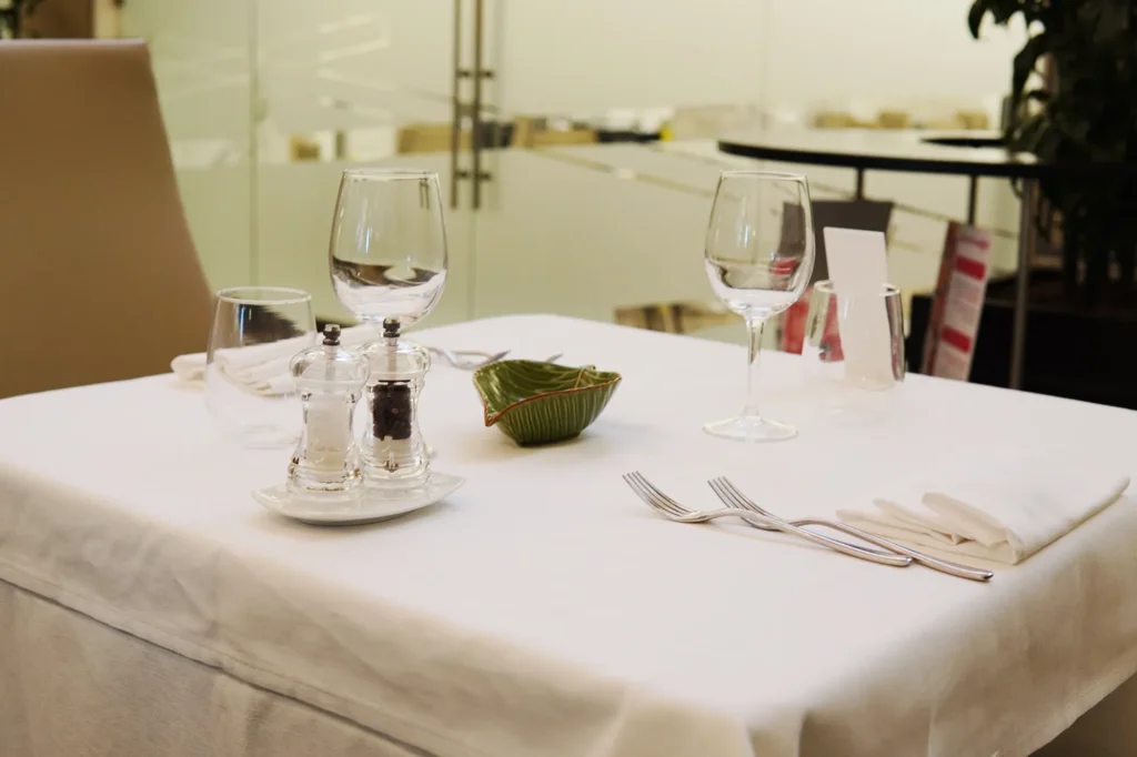 Nell'immagine il dettaglio di un tavolo della sala del ristorante apparecchiato con calici, posate, tovaglioli e spezie.